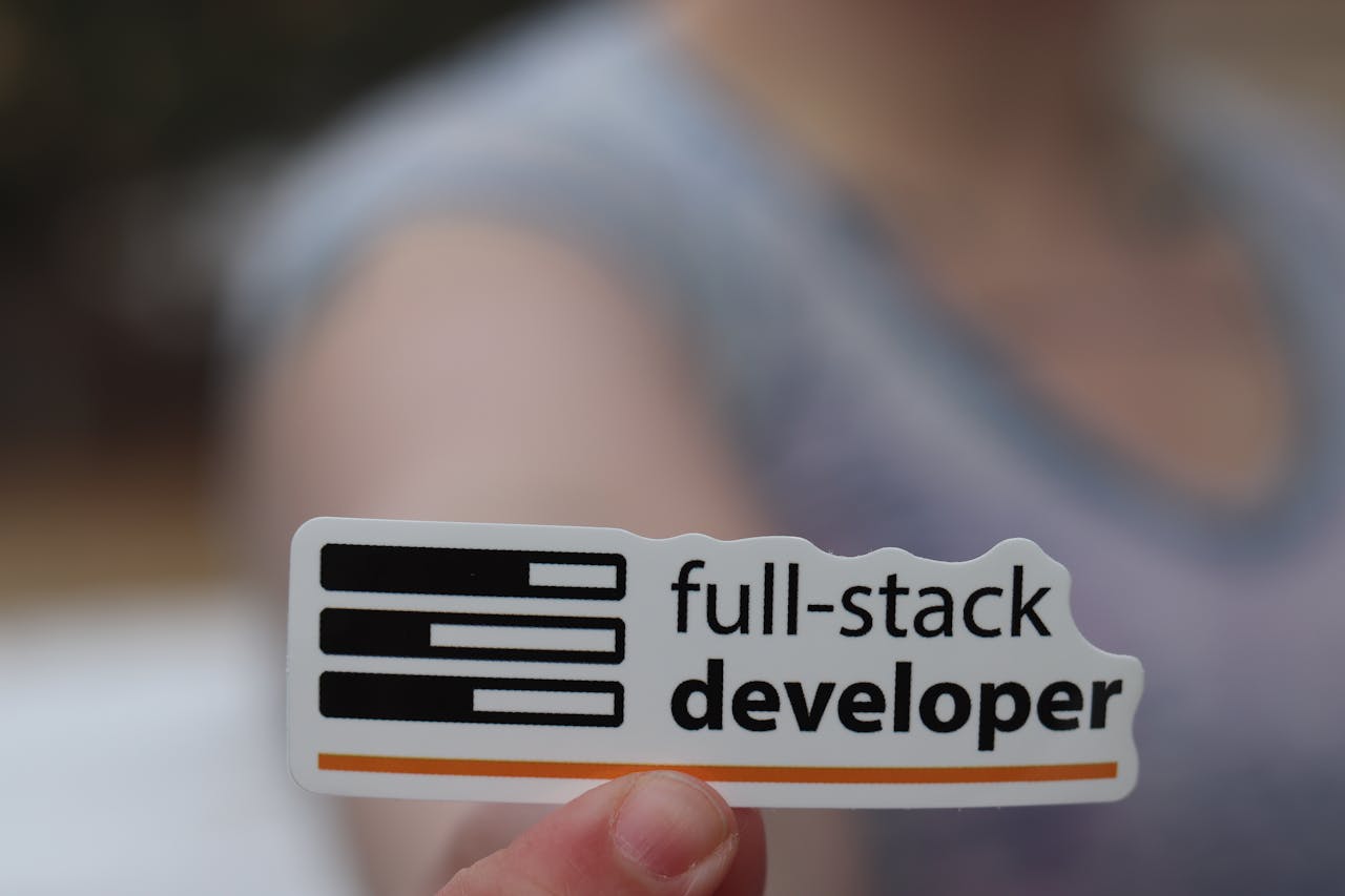 A hand holding a sticker labeled full-stack developer, symbolizing technology and programming skills.